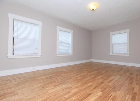 A room with wooden flooring and two windows.
