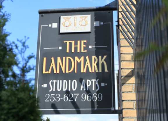 A sign for The Landmark Studio Apts with a phone number on it.