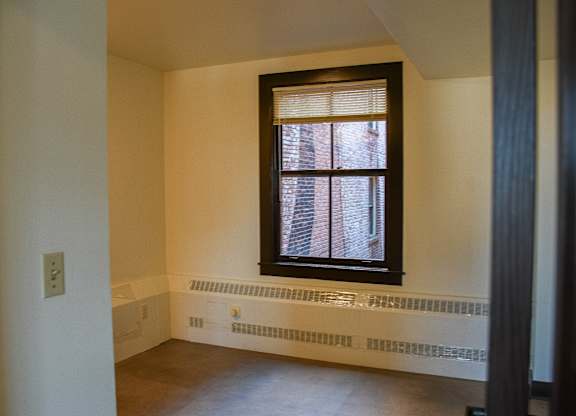 A window with blinds in a room with a white wall and a brown floor.