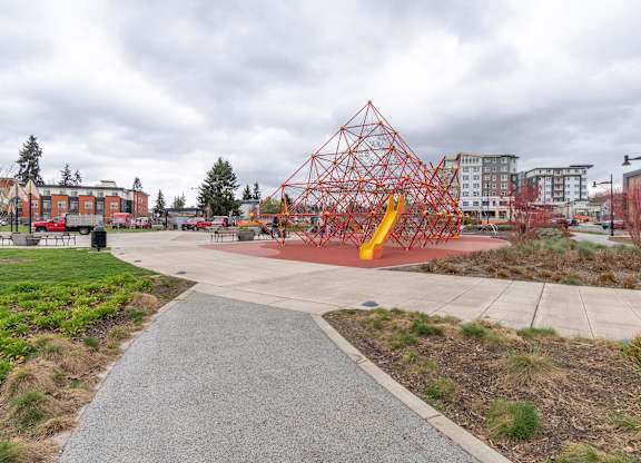 A playground with a red and yellow structure in the middle of a concrete area.