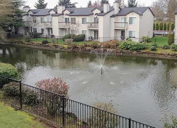 A fountain in the middle of a pond in front of a building.