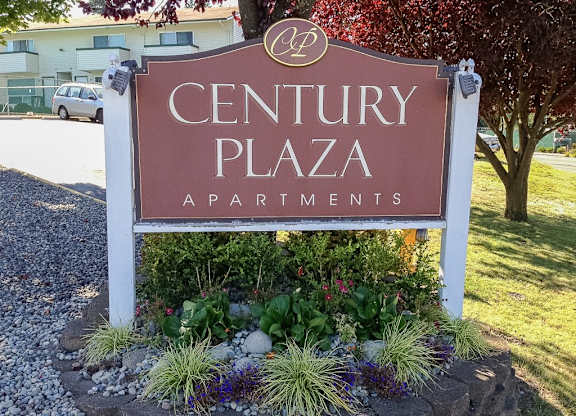 A sign for Century Plaza Apartments is surrounded by plants and flowers.