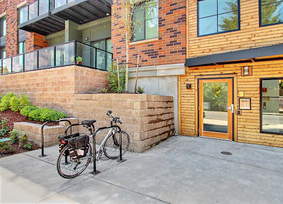A bicycle is parked on a sidewalk in front of a brick wall and a building with a glass door.