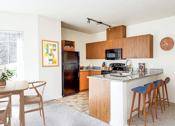 A kitchen with a refrigerator, microwave, and bar stools.