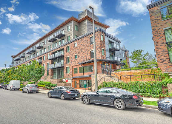 A street view of a multi-story building with cars parked in front.
