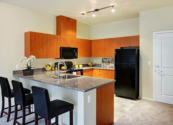 A kitchen with a granite countertop and black chairs.