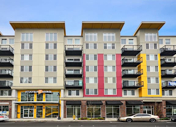 A multi-story apartment building with balconies and a storefront at the ground level.