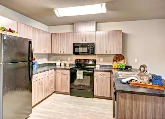 A kitchen with a black refrigerator and wooden cabinets.