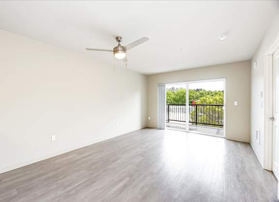 A spacious room with a ceiling fan and sliding glass doors leading to a balcony.