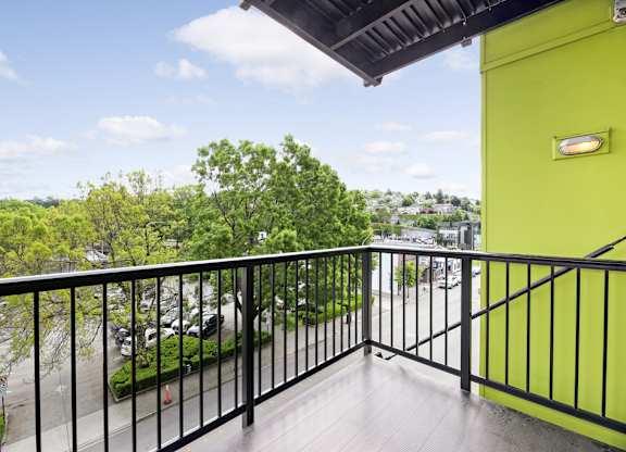 A balcony with a black railing and a view of a parking lot and trees.
