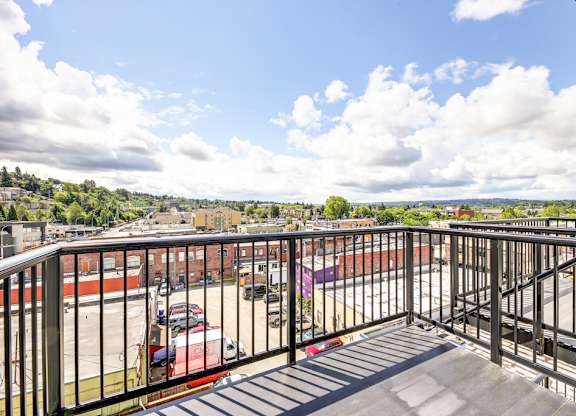 A balcony with a metal railing overlooks a parking lot and buildings.