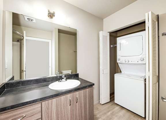 A bathroom with a sink, mirror, and a washer and dryer.