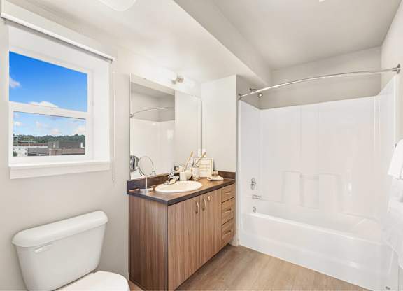 A white bathroom with a large window and a wooden vanity.