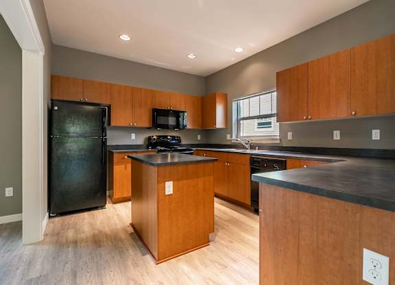 A kitchen with wooden cabinets and a black refrigerator.