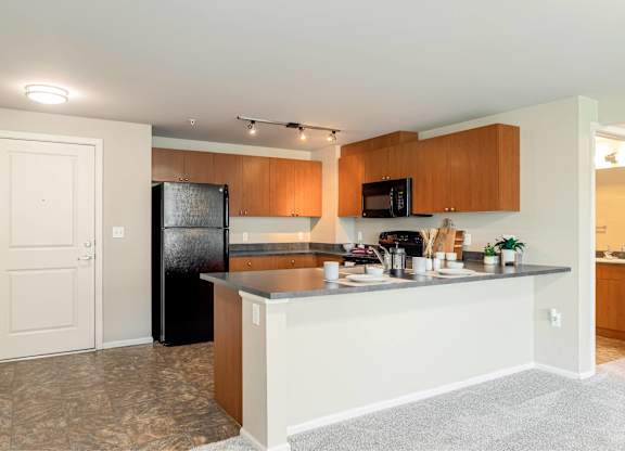 A kitchen with a black fridge and wooden cabinets.