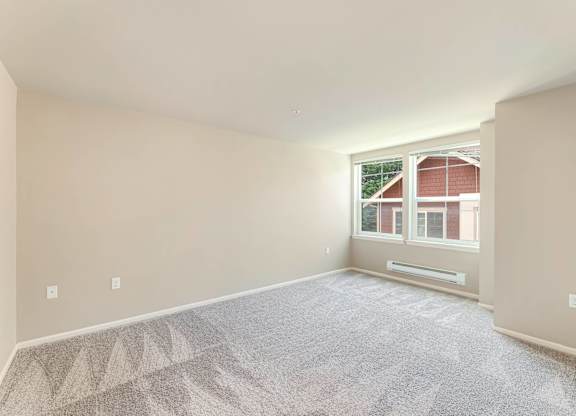 A room with a carpeted floor and a window showing a red building outside.
