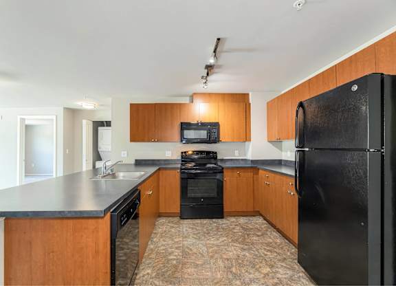 A black refrigerator is in the corner of a kitchen with wooden cabinets.