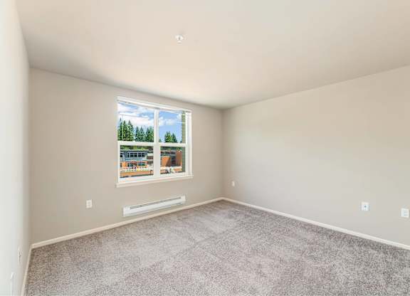 A room with a carpeted floor and a window showing a view of trees and a building outside.