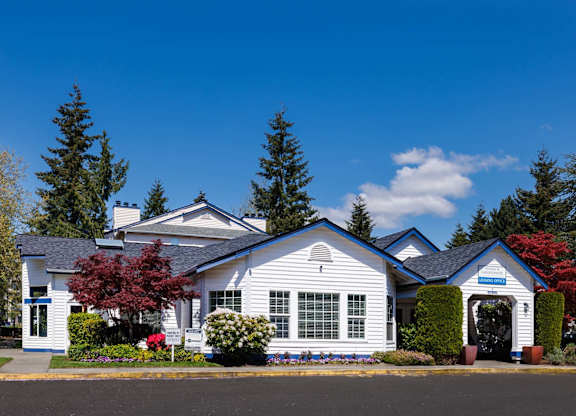 A white house with a blue roof and a red tree in front.