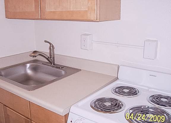 A kitchen with a stove, sink, and cabinets.