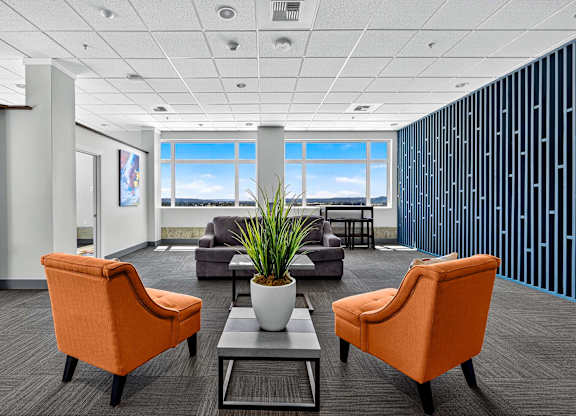 A modern office with orange chairs and a view of the sky through the window.