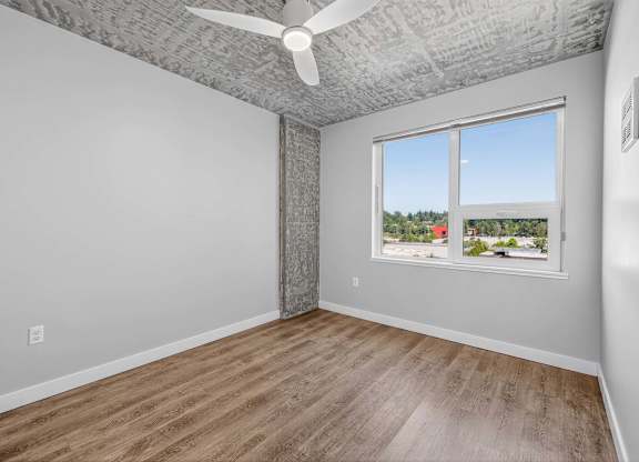 A room with a ceiling fan and a window overlooking a residential area.