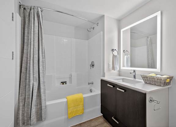 A bathroom with a white tub, sink, and a grey shower curtain.