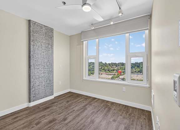 A room with a window that has a view of a red building and trees outside.