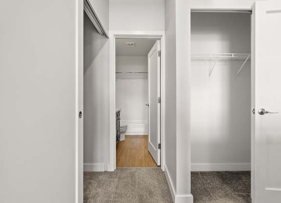 A white hallway with a door on the right and a toilet in the distance.
