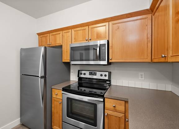 A kitchen with a stainless steel refrigerator, microwave, oven, and cabinets.