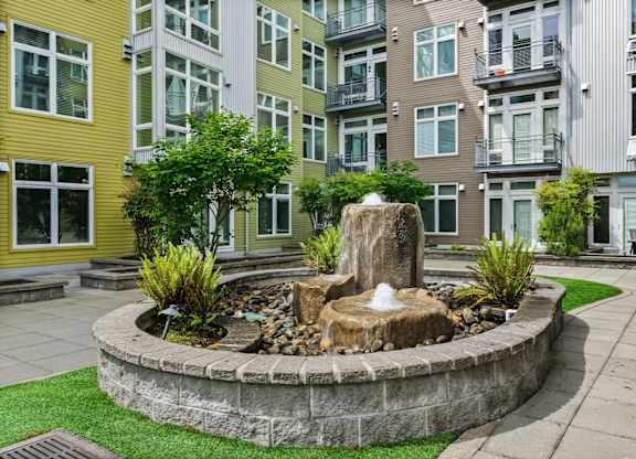 A fountain in the middle of a garden surrounded by a stone wall.