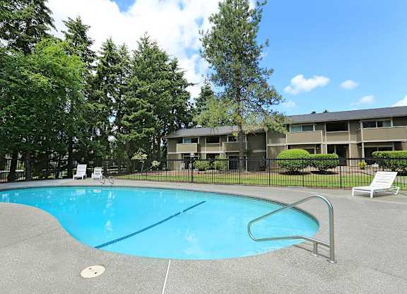 A swimming pool surrounded by trees and a building in the background.