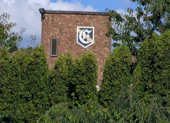 A building with a white emblem on a brick wall surrounded by green trees.