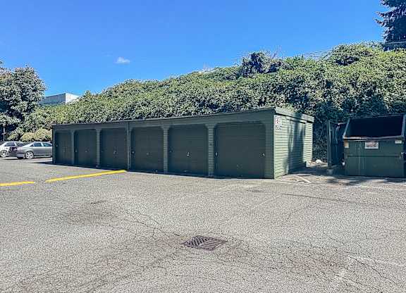 A parking lot with a row of green garages and a car parked in the background.
