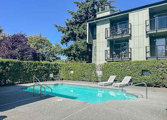 A pool with chairs and a building in the background.