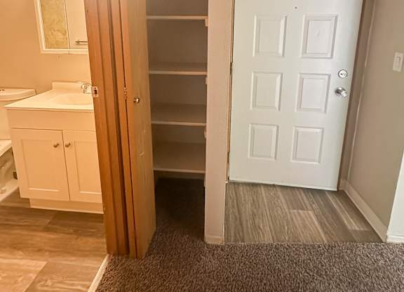 A white door is in a hallway with a white cabinet and a white sink.