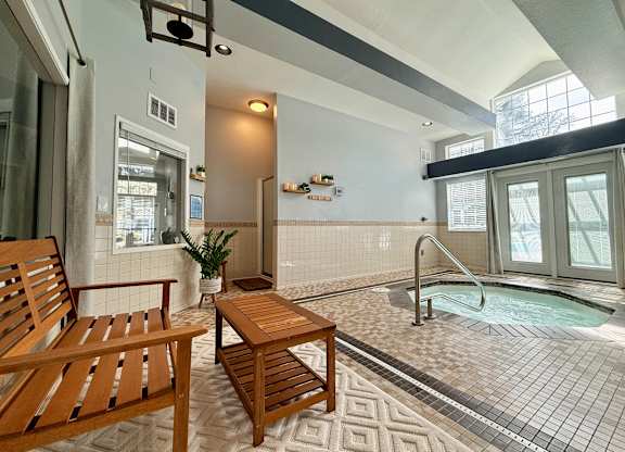 A wooden chair and table are placed in a room with a hot tub.