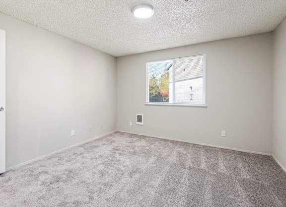 A room with a carpeted floor and a window showing a view of a house.