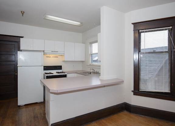 A kitchen with white appliances and a wooden floor.