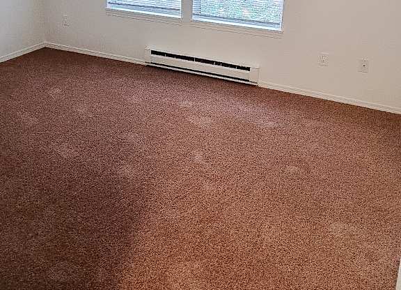 A room with a carpeted floor and a window with blinds.