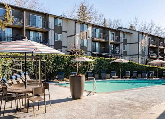 A pool area with chairs and umbrellas in front of apartment buildings.