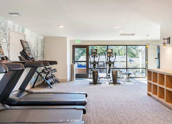 A gym with treadmills, weights, and a green exit sign.