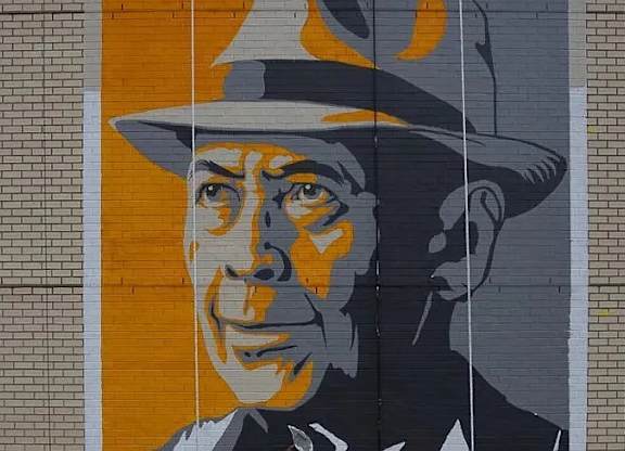 A mural of a man in a hat is painted on a brick wall.