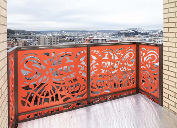 A balcony with a red railing and a view of a cityscape.