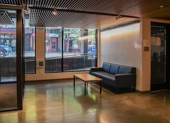 A black couch sits in a room with a wooden table in front of it.