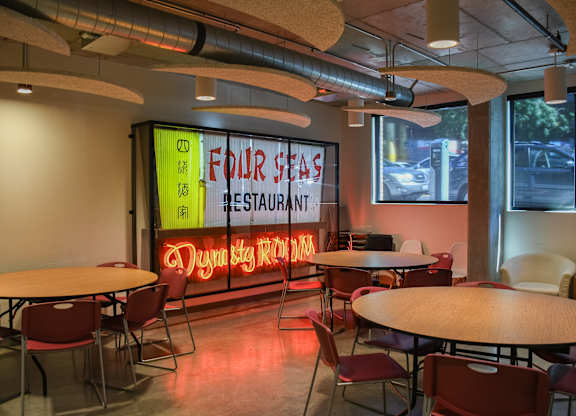 A restaurant with tables and chairs and a neon sign that says "Four Seas Restaurant".