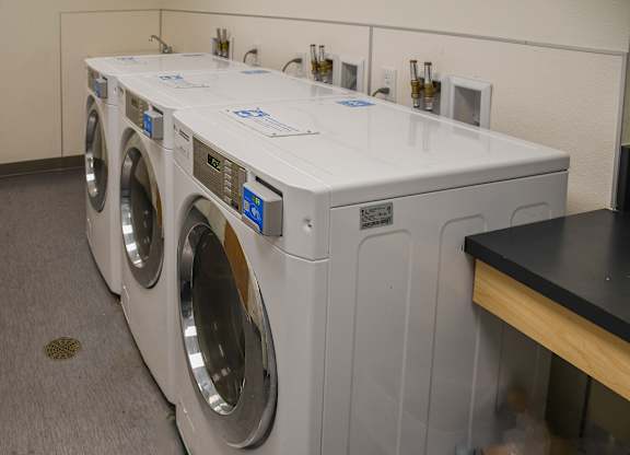 A row of white front load washing machines are lined up in a laundromat.