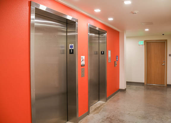 Two elevators are located in a hallway with orange walls.