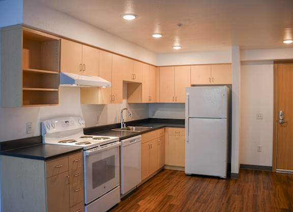 A kitchen with a white stove top oven, white refrigerator, and wooden cabinets.