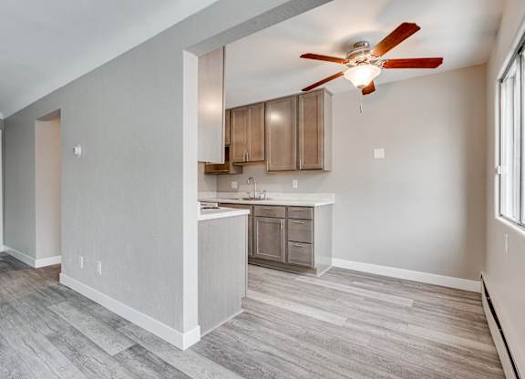 A room with a ceiling fan and a kitchen area in the background.